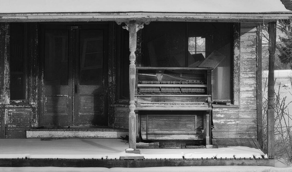 Out of Tune with Time Black and white photo of an old piano on a porch of an old building in winter